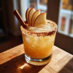 A refreshing apple cider margarita with cinnamon rim, apple slices, and a cinnamon stick garnish.
