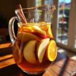 A glass pitcher filled with apple cider sangria, featuring apple and orange slices, and cinnamon sticks.