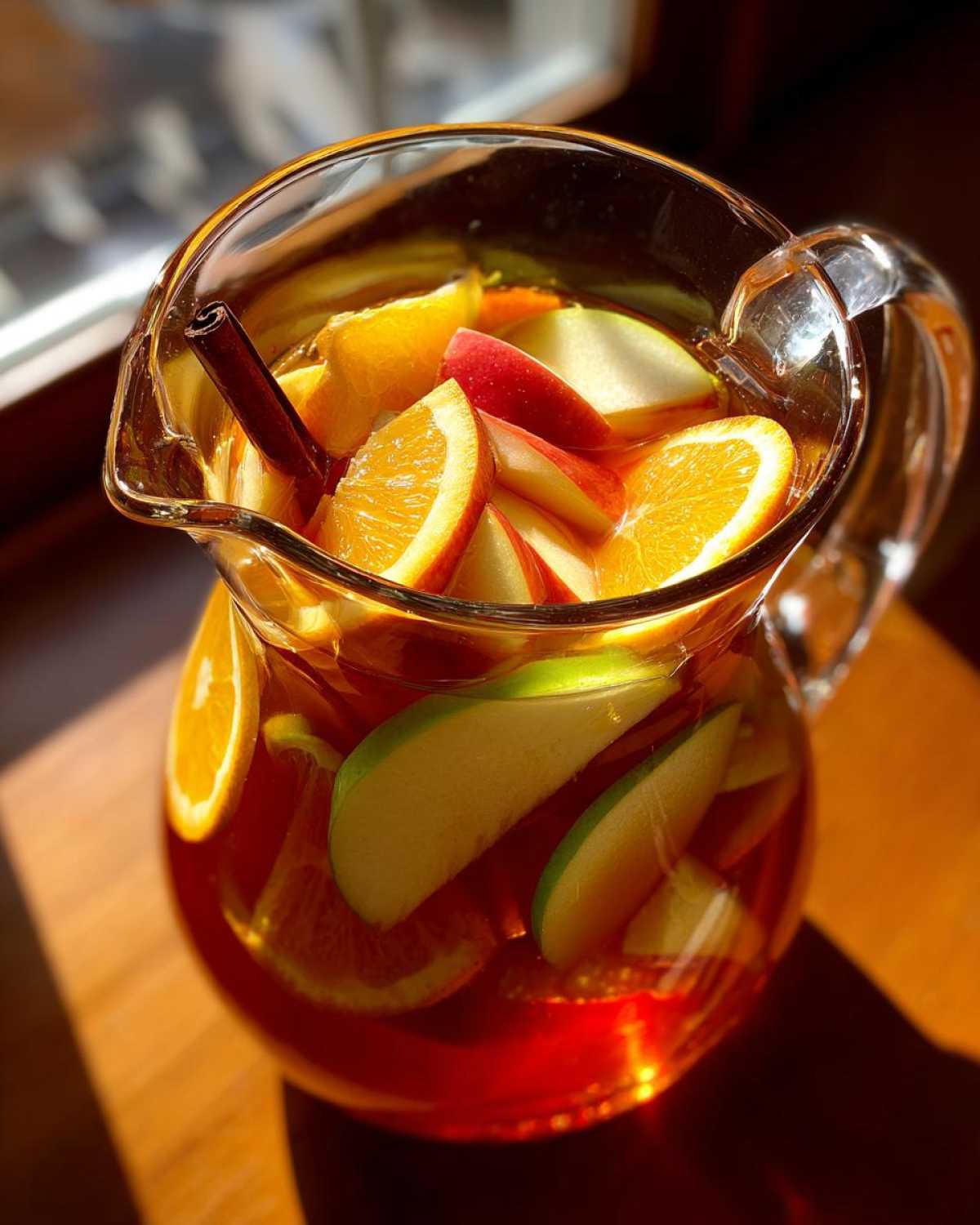 A glass pitcher filled with apple cider sangria, featuring apple and orange slices and a cinnamon stick.