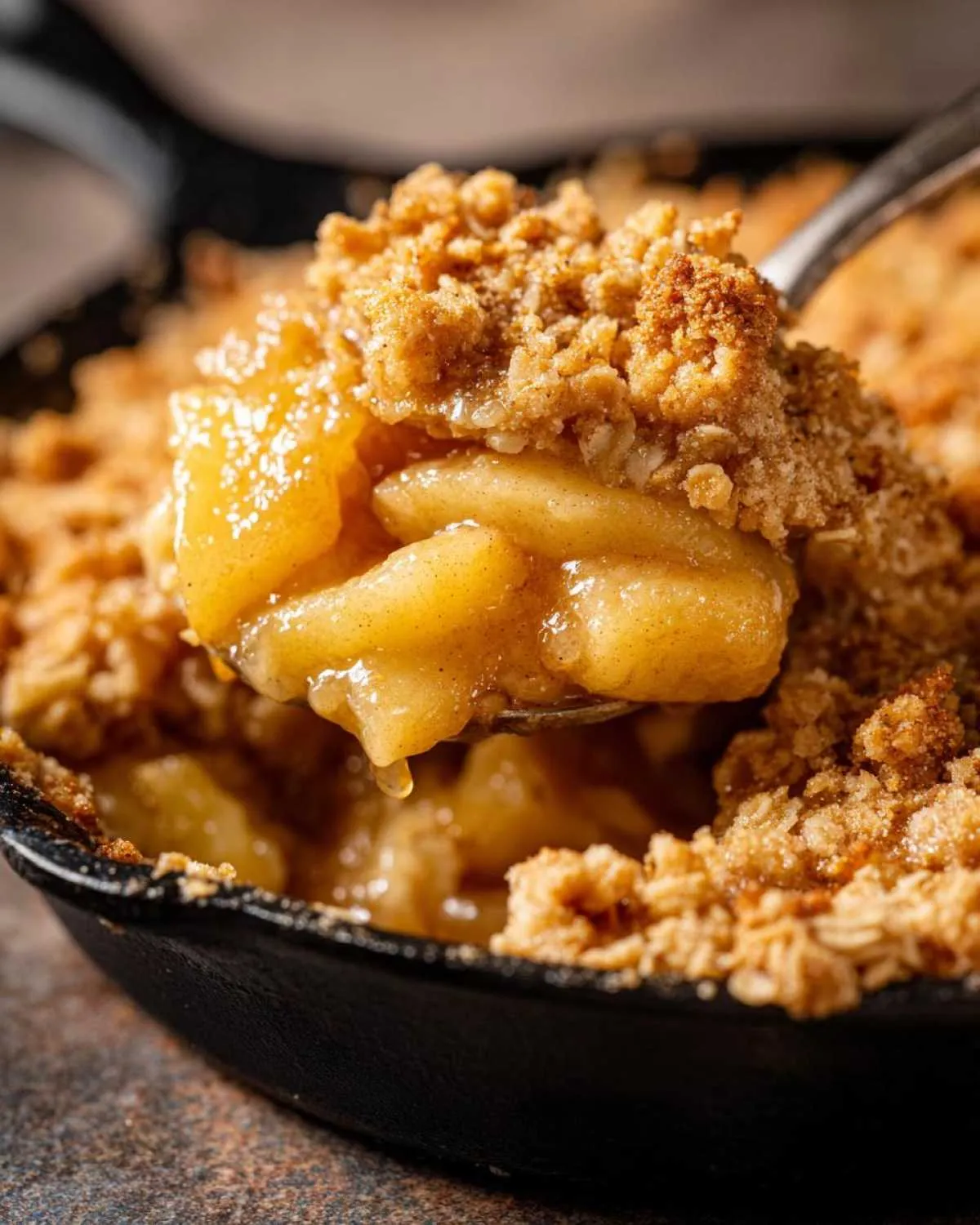 A spoonful of warm apple crisp with a golden oat topping, dripping with sweet apple juices.