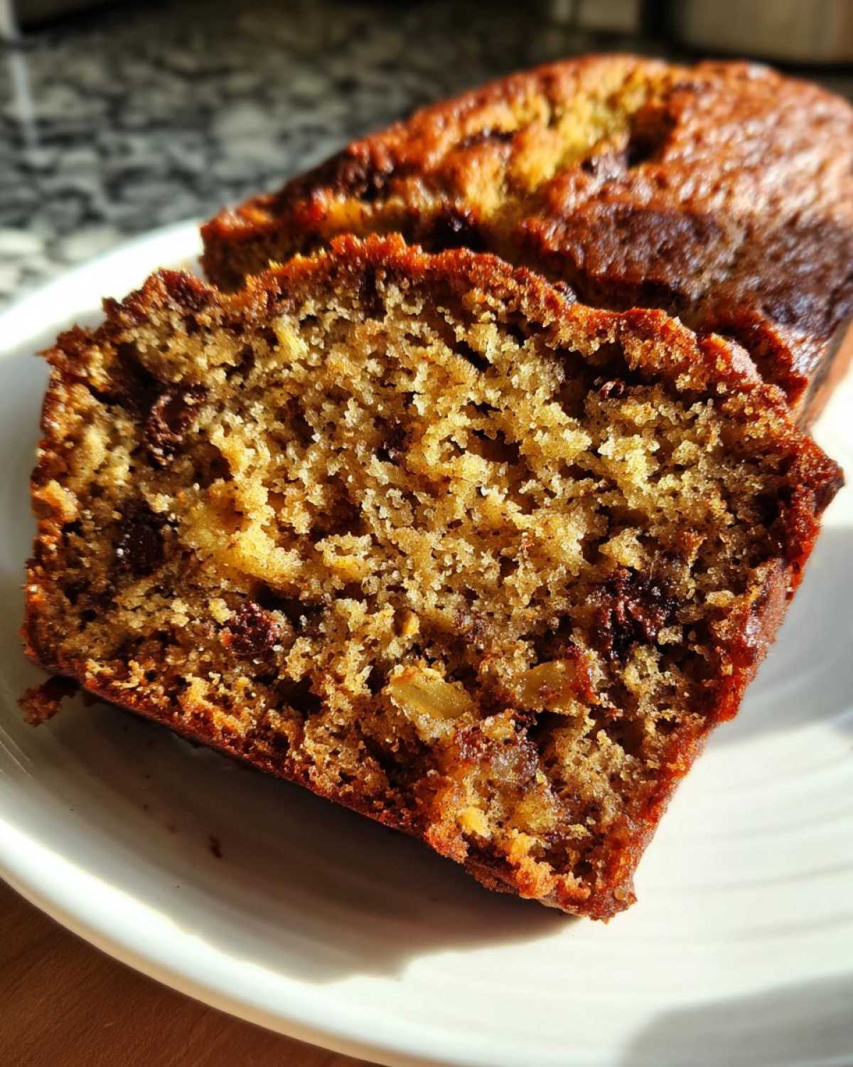 Close-up of a slice of moist banana zucchini bread with chocolate chips on a white plate.