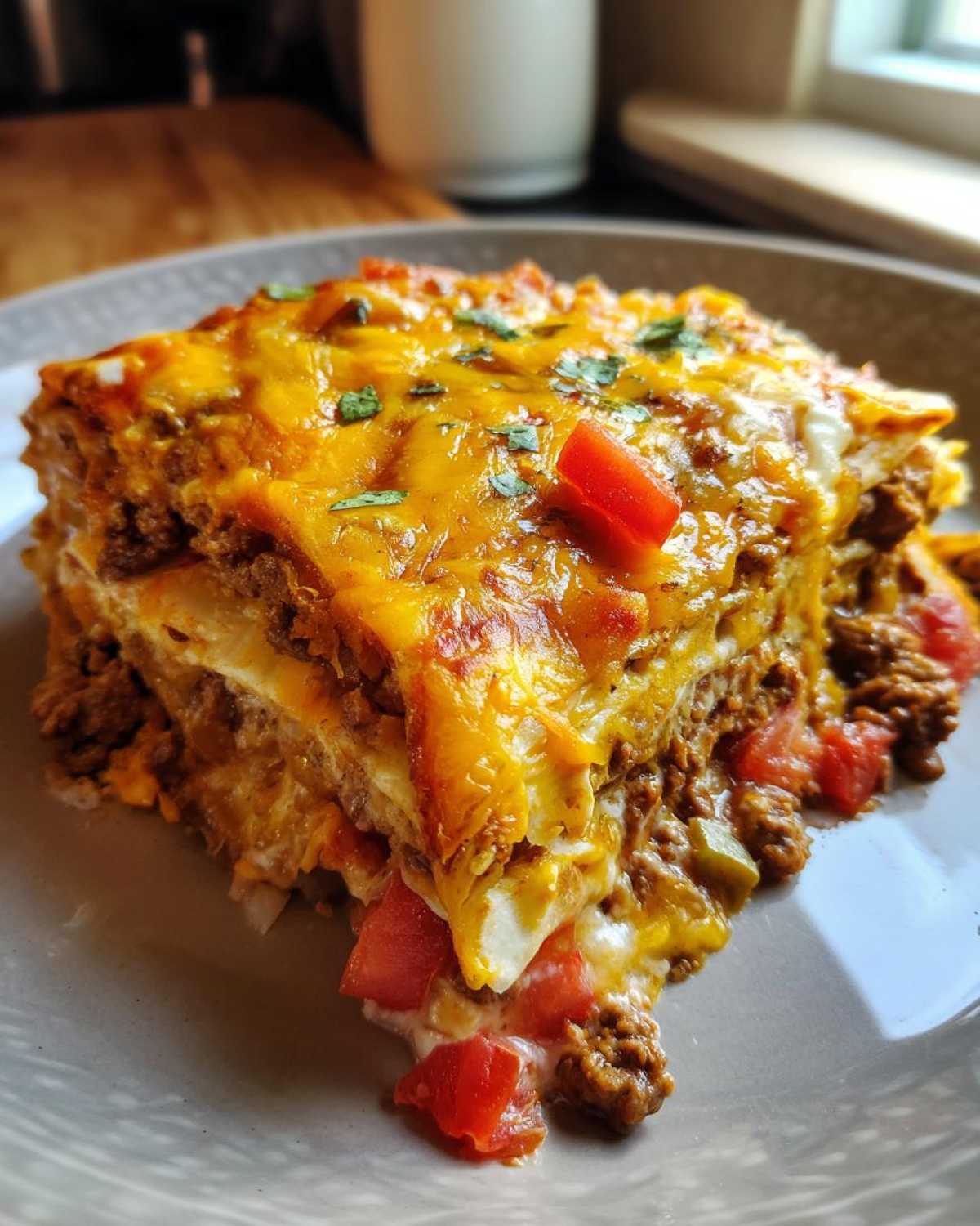 A slice of cheesy burrito bake with layers of tortillas, ground beef, tomatoes, and melted cheese.