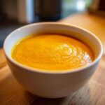 A bowl of vibrant butternut squash soup, smooth and creamy, served in a white bowl.