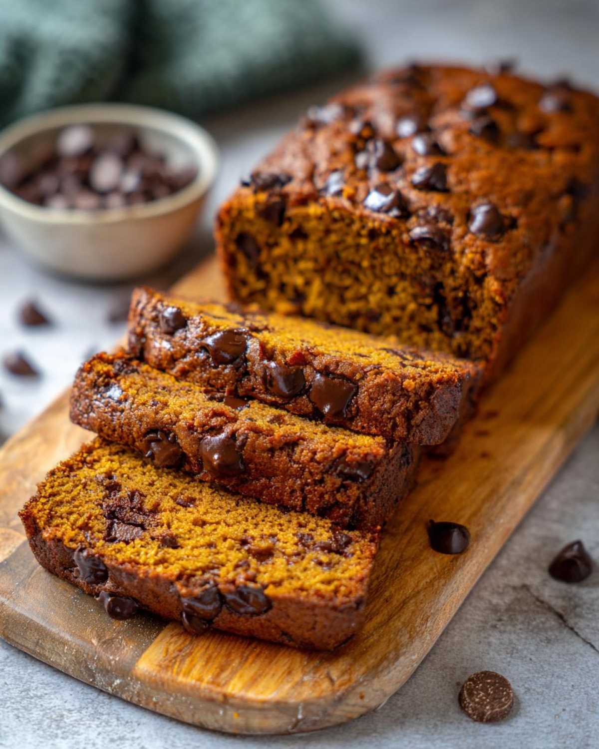 Close-up of sliced chocolate chip pumpkin bread loaf on a wooden board, with chocolate chips.