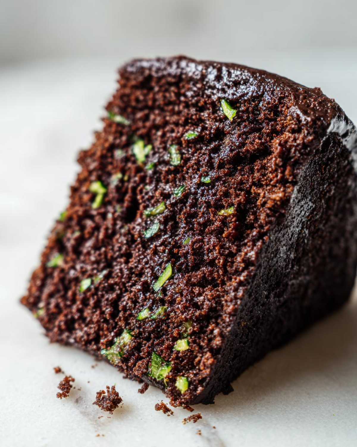 A delicious slice of chocolate zucchini cake showing the moist texture and flecks of zucchini.