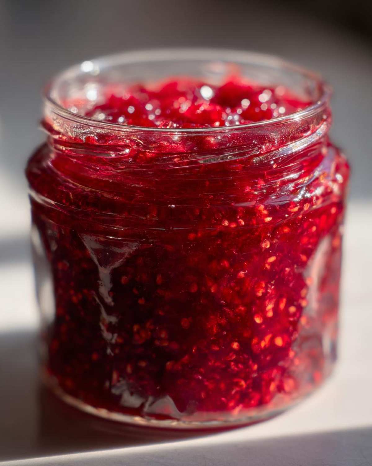 Close-up of a jar filled with vibrant red Christmas jam, showcasing its rich texture and color.