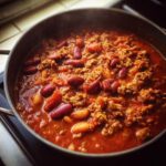 A pot of delicious crockpot chili with kidney beans, ground meat, and tomatoes, simmering on the stove.