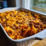 A freshly baked Dorito Casserole in a white baking dish, topped with melted cheese and seasoned ground beef.