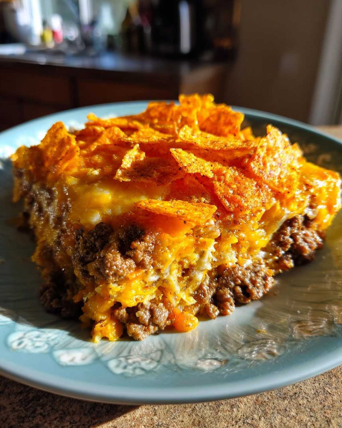 A slice of Dorito Casserole on a plate, showcasing layers of ground beef, cheese, and crushed Doritos.