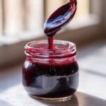 A spoonful of dark purple elderberry syrup being poured into a glass jar, showcasing a homemade elderberry syrup recipe.
