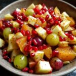 Close-up of a colorful fall fruit salad in a bowl, featuring apples, oranges, grapes, and pomegranate seeds.