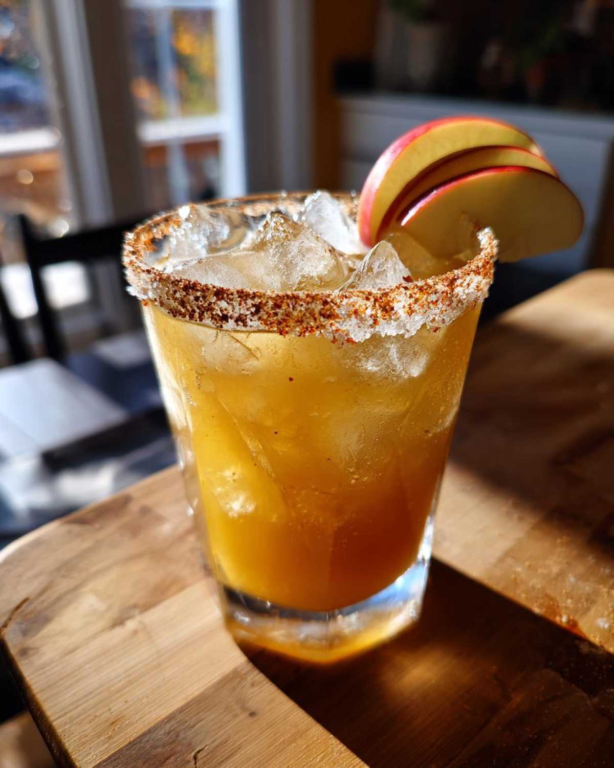 A vibrant fall margarita in a glass with a spiced rim, ice, and apple slice garnish.