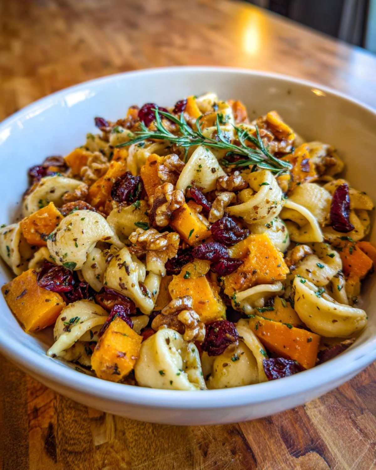 A vibrant bowl of fall pasta salad with butternut squash, cranberries, walnuts, and fresh herbs.