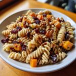 A vibrant bowl of fall pasta salad featuring rotini pasta, butternut squash, cranberries, and walnuts.