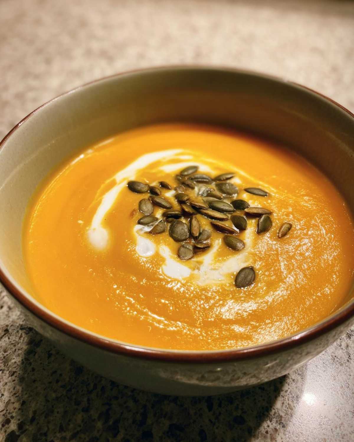 A bowl of vibrant orange fall soup, garnished with cream and pumpkin seeds, ready to be enjoyed.