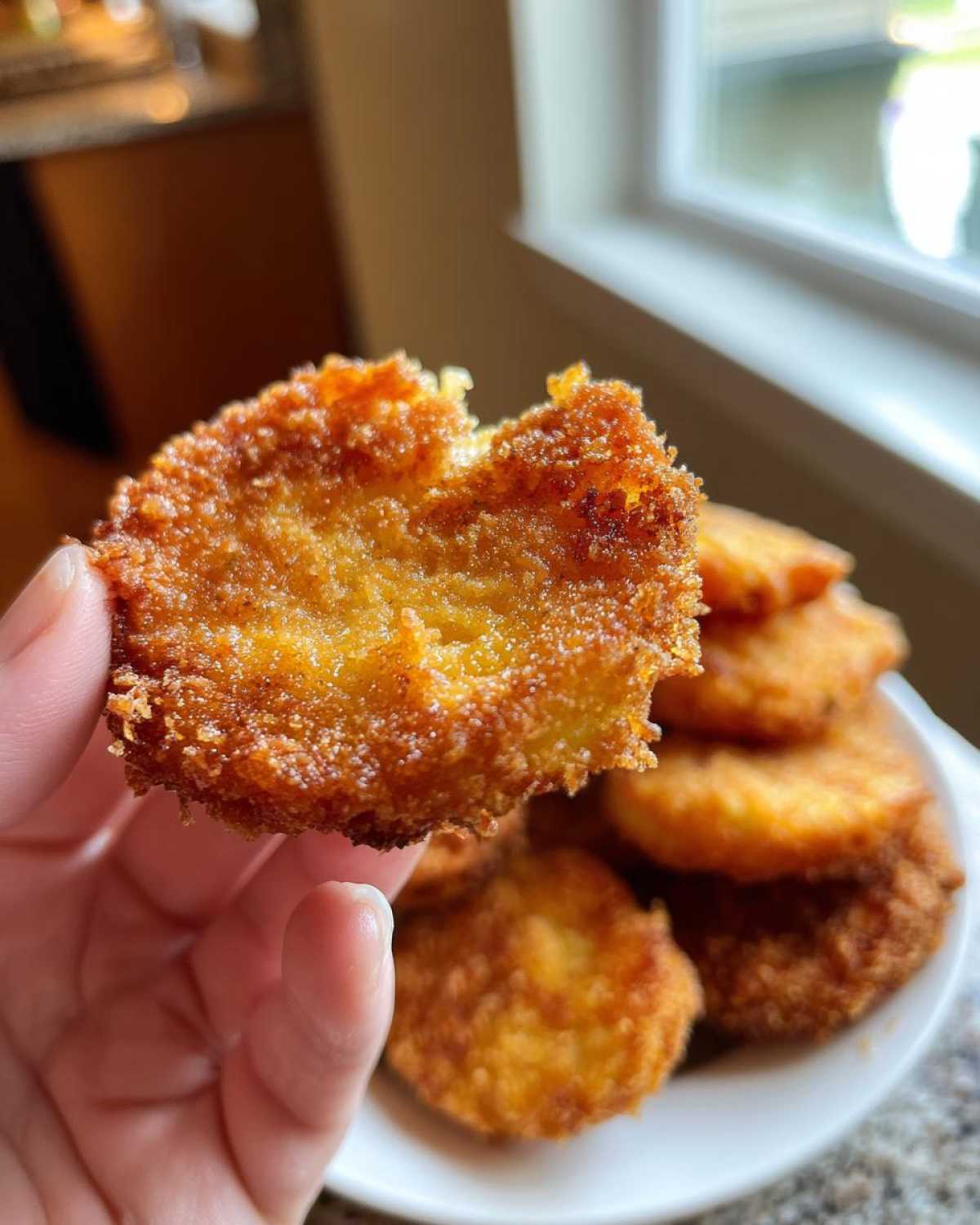 A hand holds a bite of fried green tomatoes, showing the crispy texture and juicy interior.