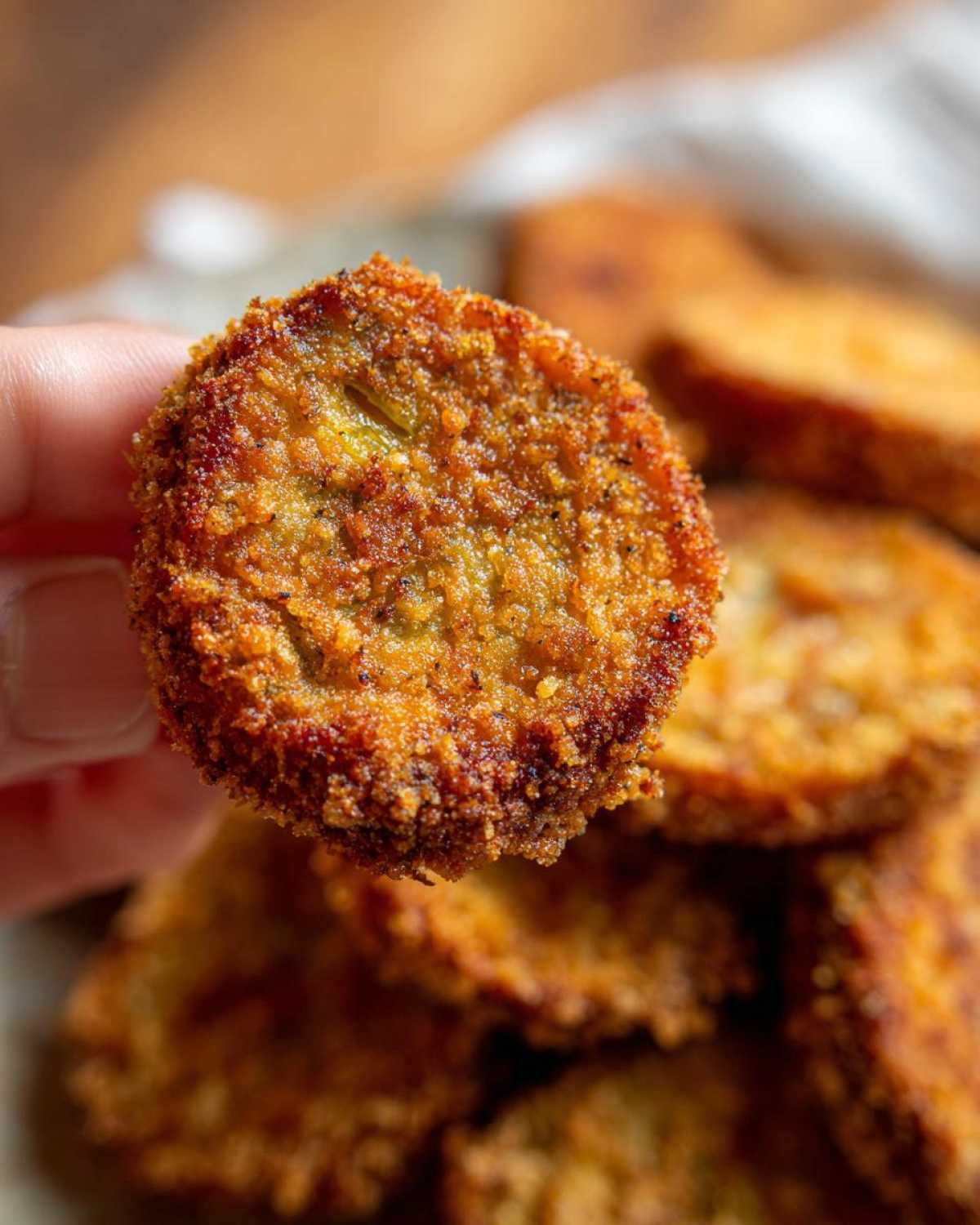 Close-up of a golden fried green tomato held in a hand, showcasing its crispy texture.