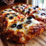Close-up of Halloween pizza slices topped with melted cheese and black olive spiders on a wooden board.