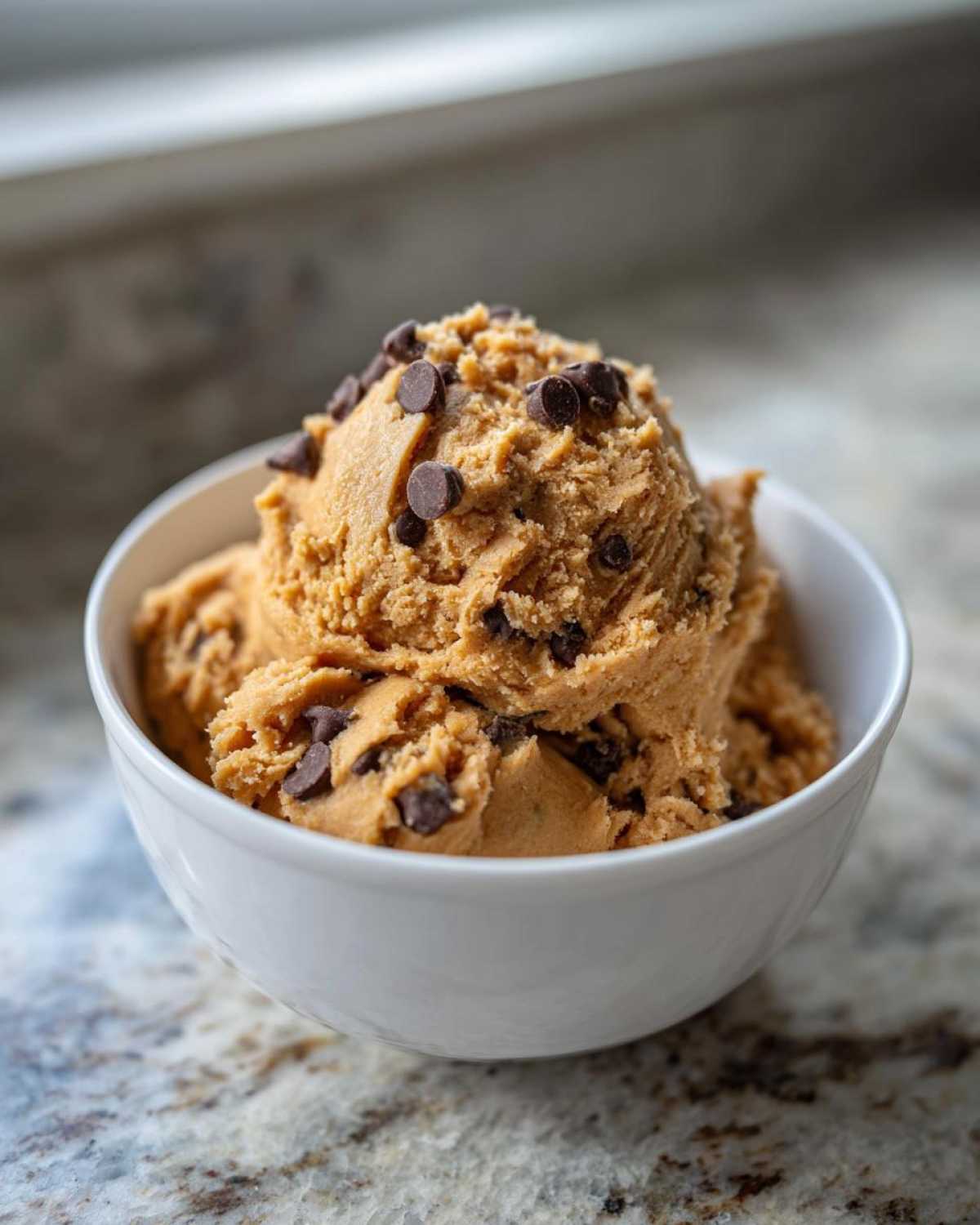 A white bowl filled with delicious high protein cookie dough, topped with chocolate chips.