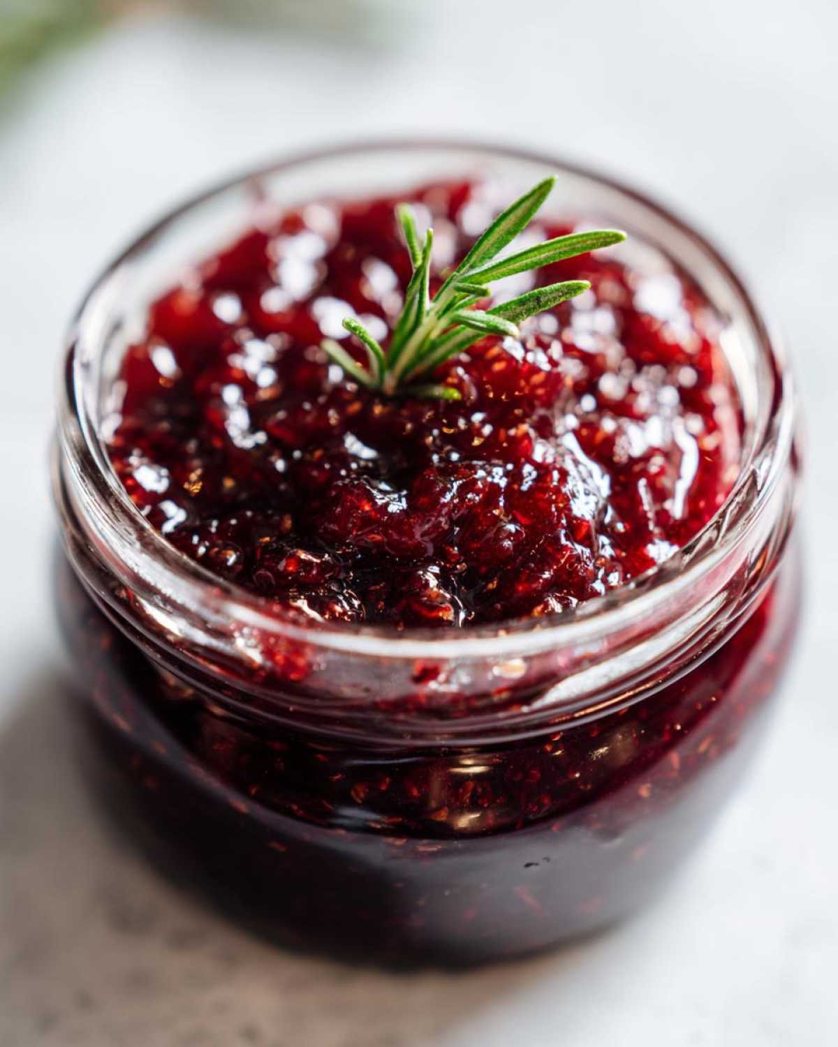 Close-up of homemade fig jam in a clear glass jar, garnished with a sprig of rosemary.