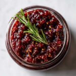 Overhead view of a jar of homemade fig jam, garnished with a sprig of rosemary.