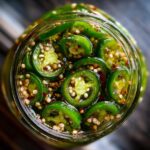 Overhead view of a glass jar filled with sliced pickled jalapenos, seeds, and spices.