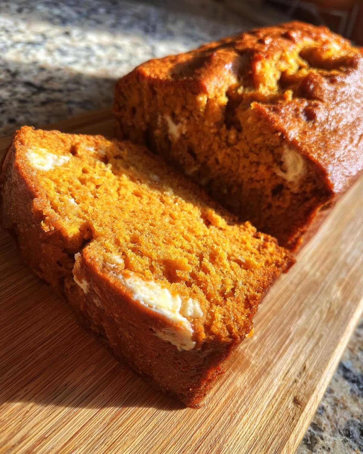 A sliced moist pumpkin loaf with cream cheese filling on a wooden board, showcasing its texture and color.