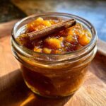 Close-up of a jar of pear preserves topped with a cinnamon stick, showcasing the homemade canning process.