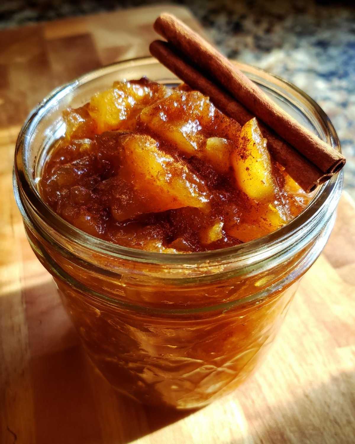 Close-up of a jar filled with homemade pear preserves, garnished with cinnamon sticks.