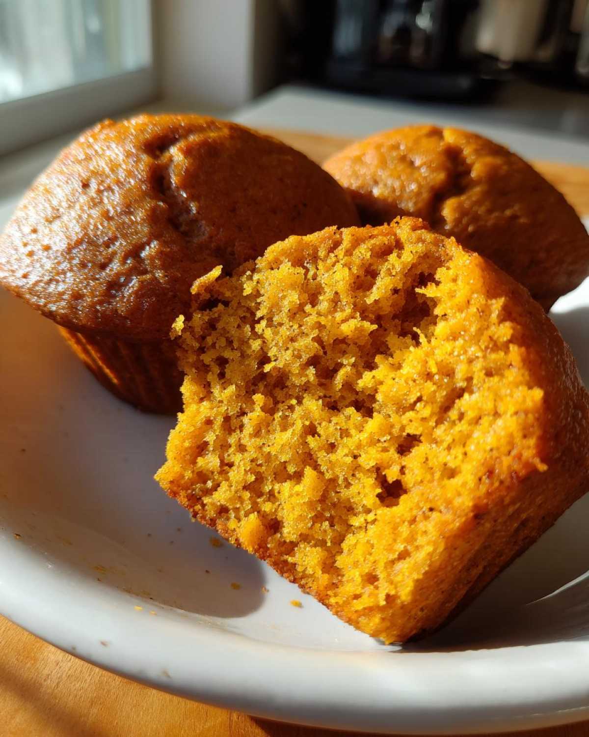 Three protein pumpkin muffins on a plate, one muffin broken open to show the texture.