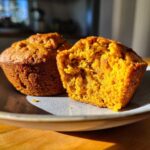 Two protein pumpkin muffins on a plate, one cut in half to show the texture.