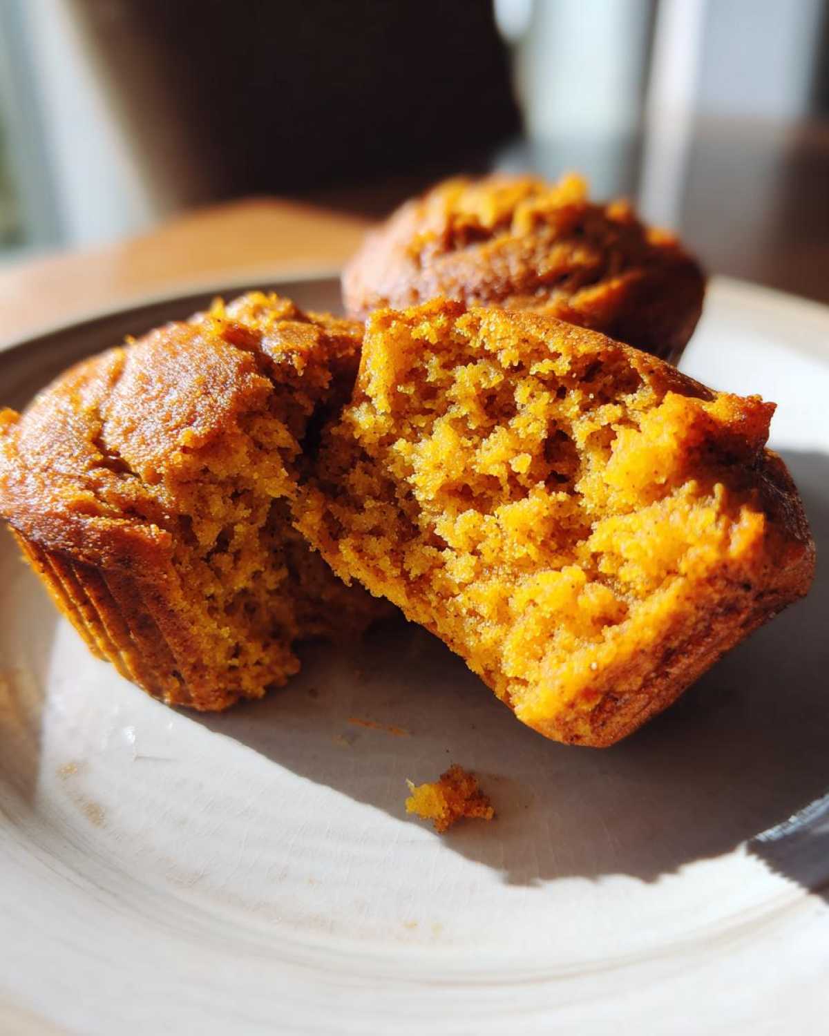 A halved protein pumpkin muffin on a plate, showcasing its moist interior. More muffins are in the background.
