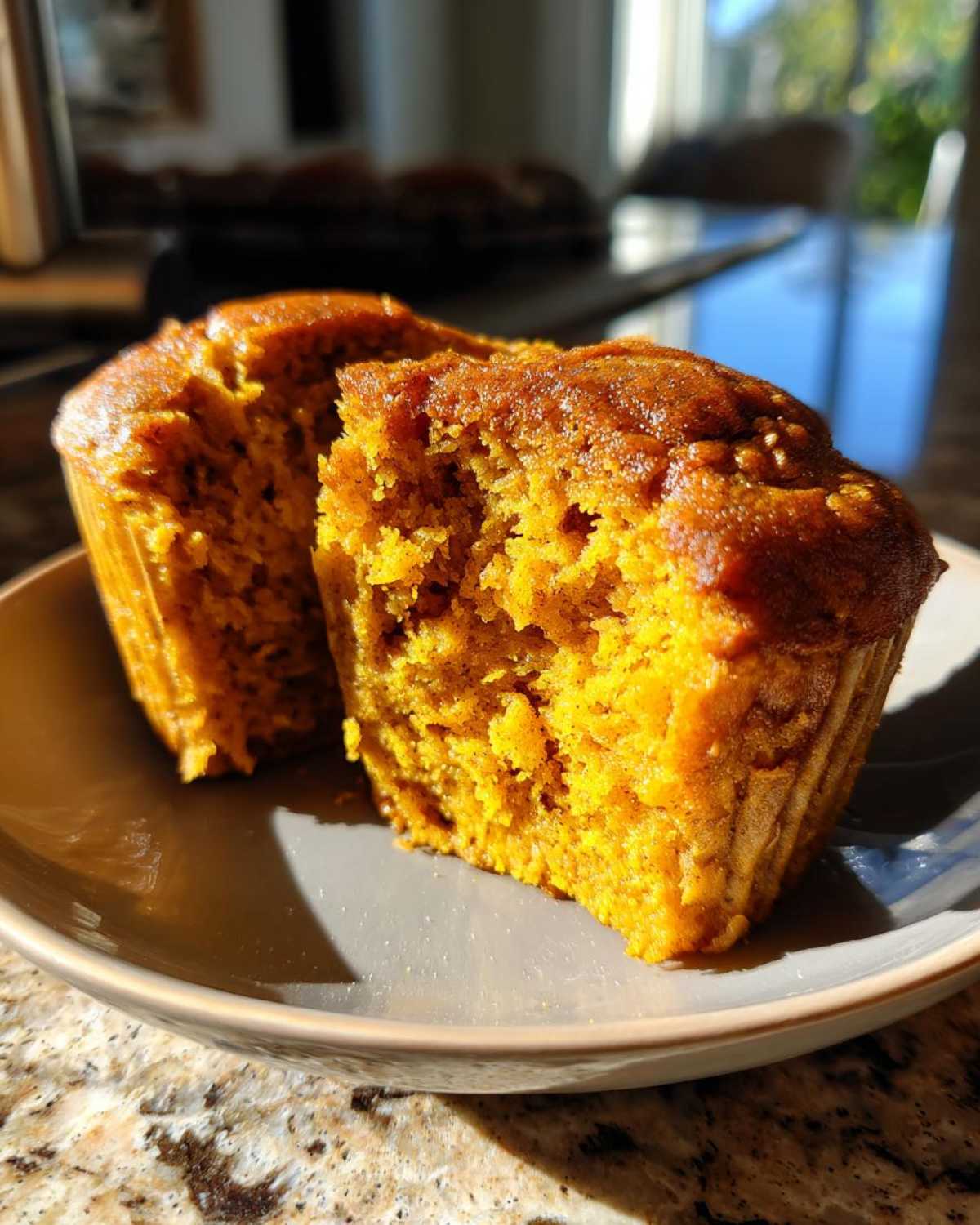 A halved protein pumpkin muffin on a plate, showcasing its moist texture and vibrant color.