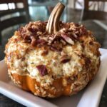A delicious pumpkin cheese ball, shaped like a pumpkin, topped with nuts and bacon, on a white plate.