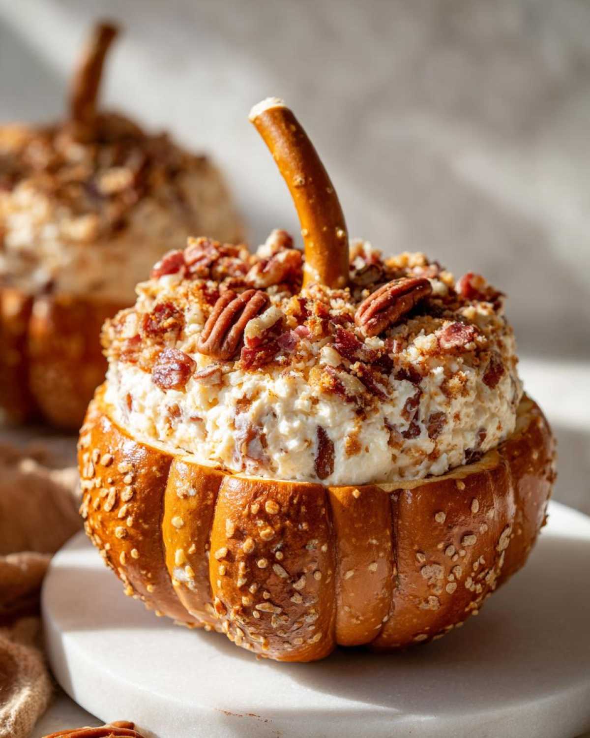 Close-up of a pumpkin cheese ball appetizer with pretzel stem, bacon, and pecans.
