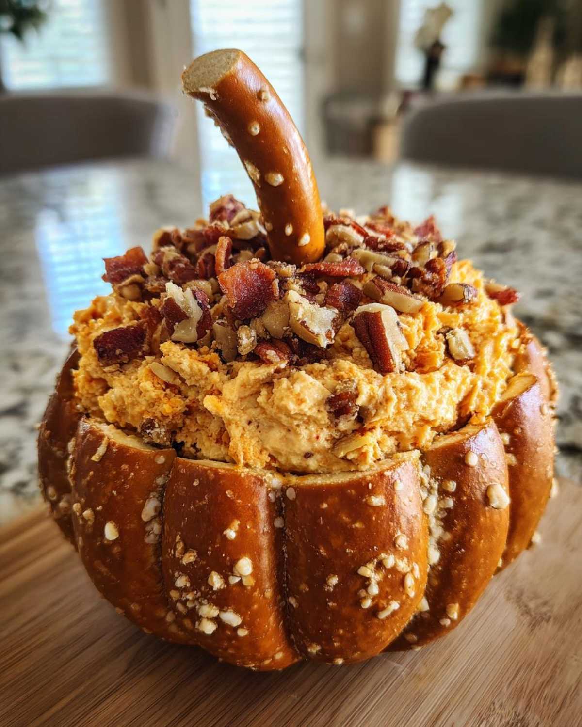 A pumpkin cheese ball served in a pretzel bowl, topped with bacon and nuts, with a pretzel stick stem.