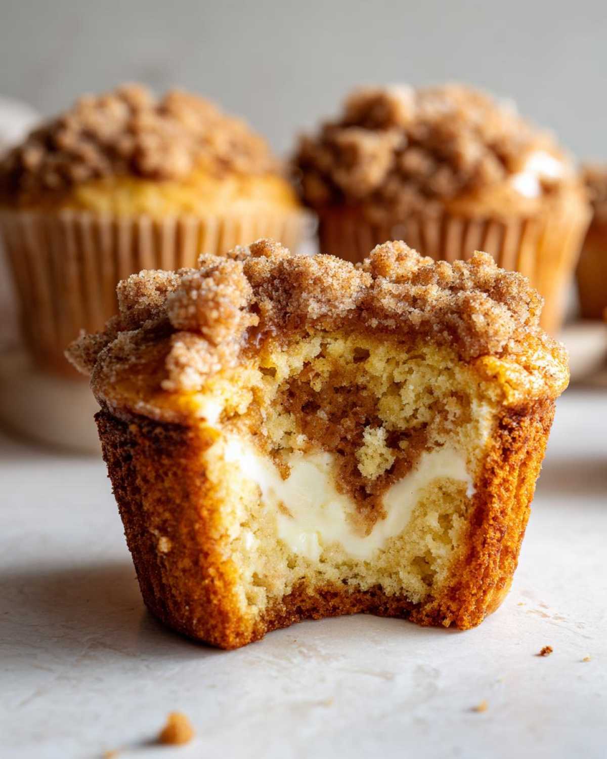 A cut pumpkin cheesecake muffin shows the cream cheese filling and crumb topping.