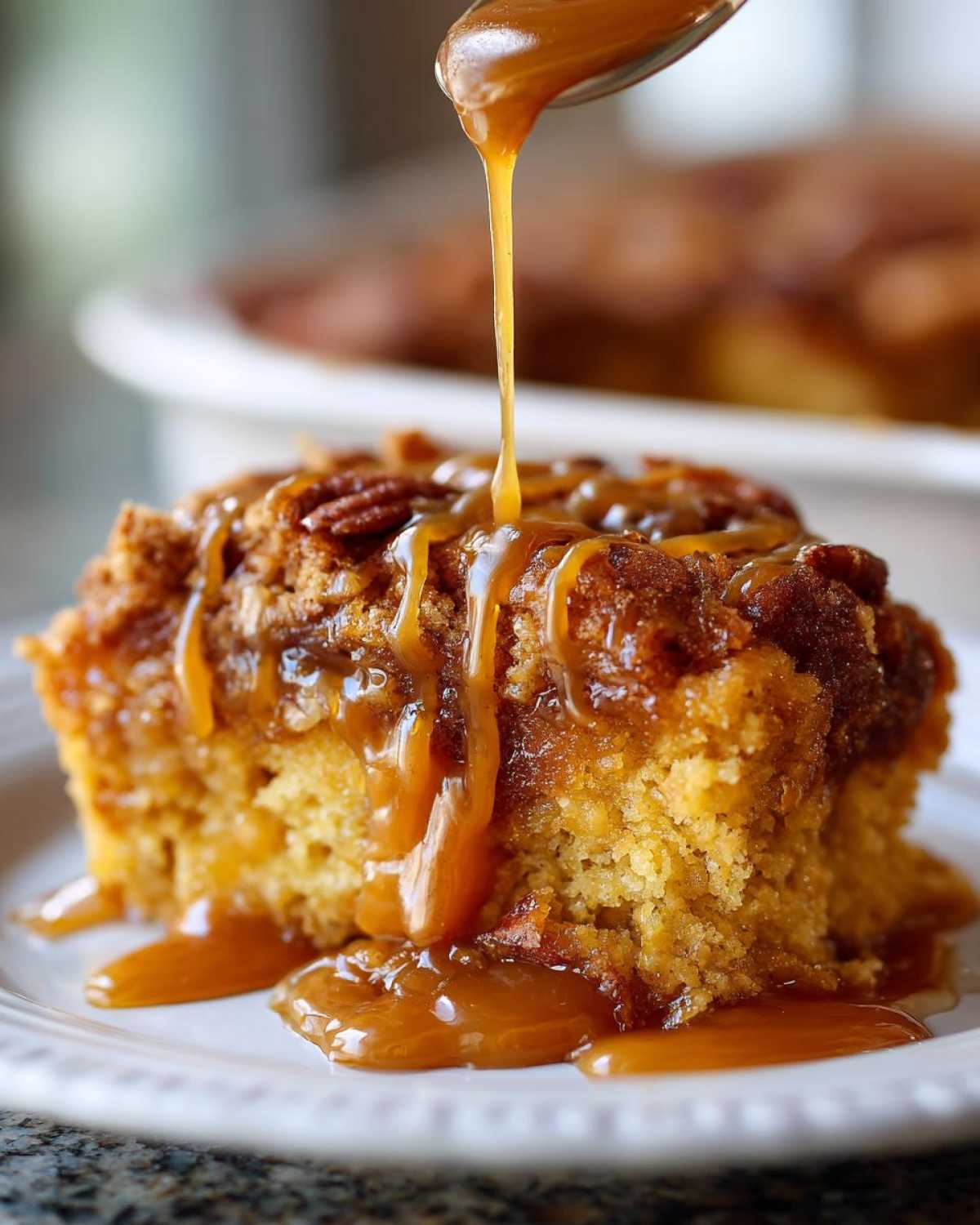 A slice of pumpkin cobbler with caramel being drizzled on top. Pecans are visible on the pumpkin cobbler.