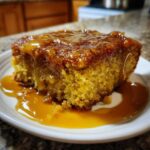 A slice of pumpkin cobbler with a gooey caramel topping, served on a white plate.