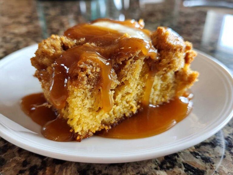 A slice of pumpkin cobbler on a white plate, topped with caramel sauce and a dollop of cream.