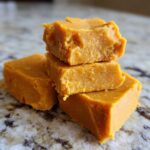 A stack of three homemade pumpkin fudge squares on a speckled surface. Close-up shot.