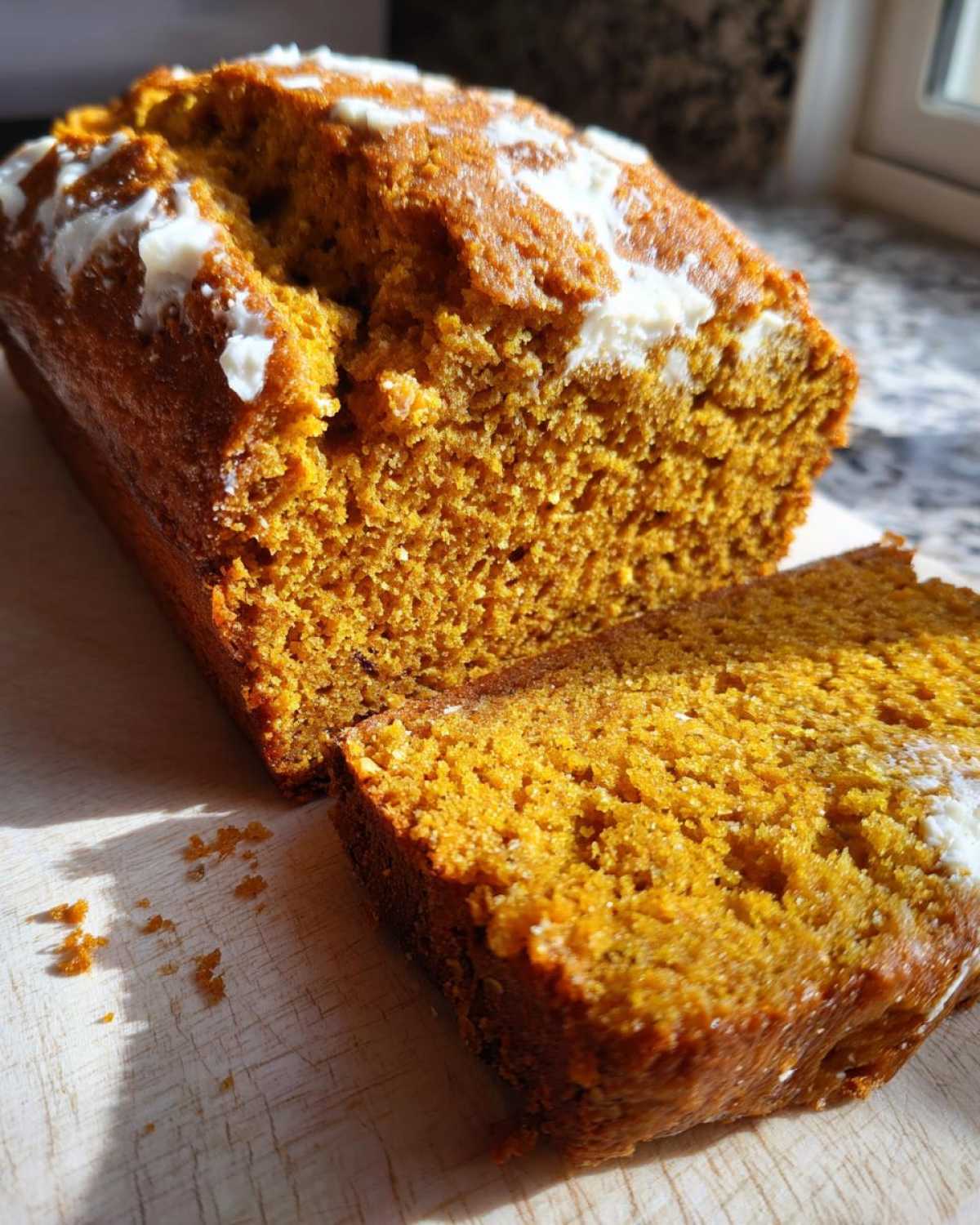 A slice of moist pumpkin loaf with butter on a wooden board, ready to eat.