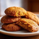 A stack of homemade pumpkin pie cookies on a plate, one cookie broken in half to show the texture.