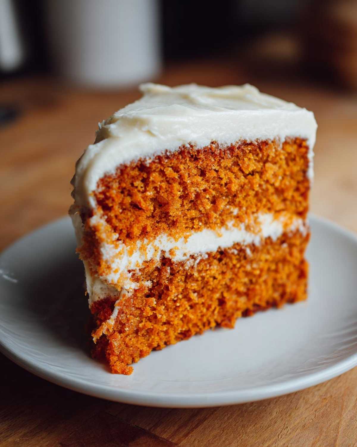 A delicious slice of pumpkin spice cake with creamy white frosting on a white plate.