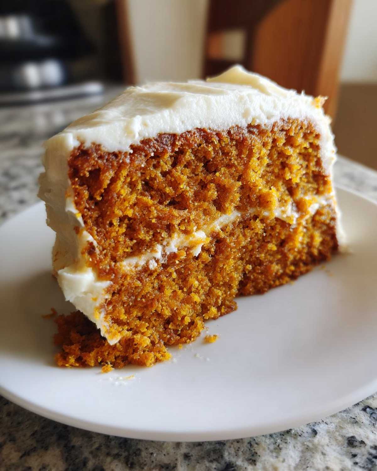 A delicious slice of pumpkin spice cake with creamy white frosting on a white plate.
