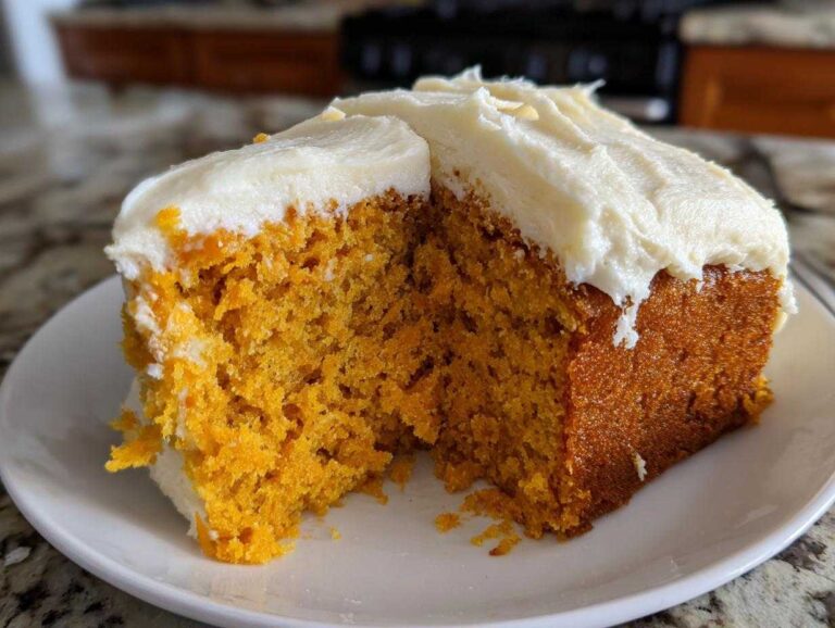 A slice of moist pumpkin spice cake with creamy white frosting on a white plate.