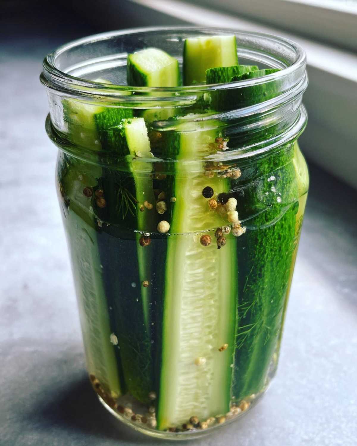A glass jar filled with crisp refrigerator pickles, showing cucumber spears and cubes in brine with spices.