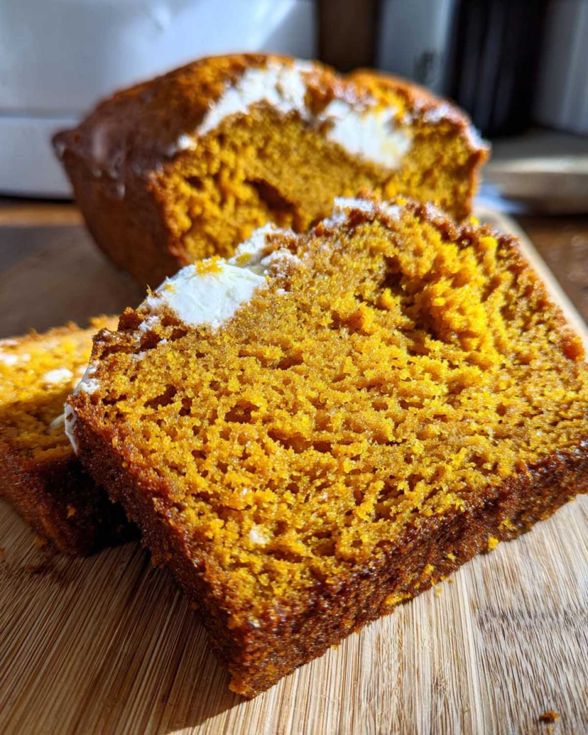 Close-up of sliced pumpkin loaf with cream cheese frosting on a wooden board.