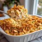 Spoonful of Tuna Casserole being lifted from a baking dish, showing the creamy filling and crispy topping.