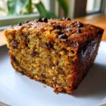 A delicious slice of zucchini banana bread topped with chocolate chips, served on a white plate.